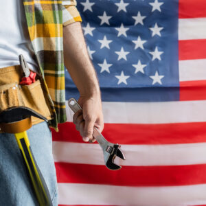 partial view of builder in tool belt holding wrench near usa flag on background, labor day concept